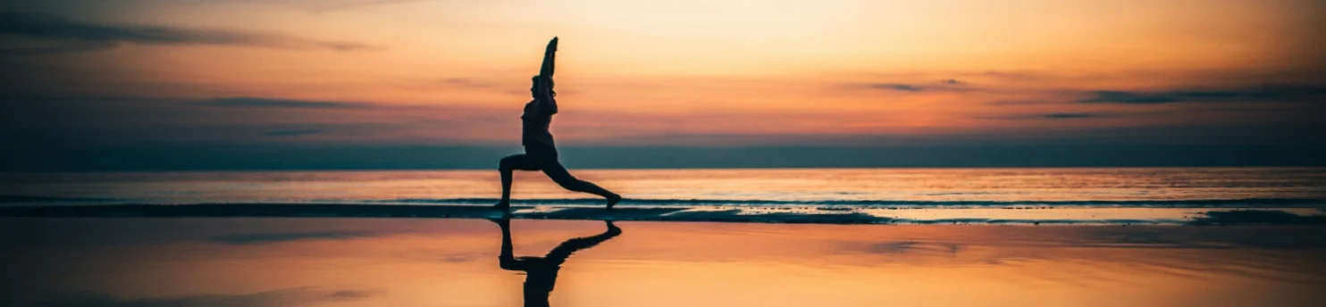 Bild von einer Person, die am Strand vor dem Meer Yoga macht. 