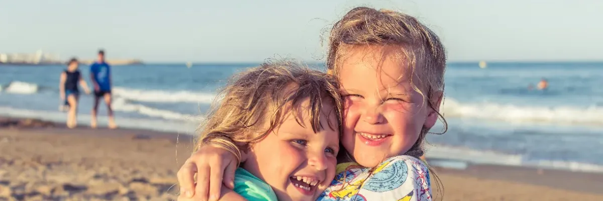 Zwei lachende Kinder umarmen sich am Strand von Fehmarn