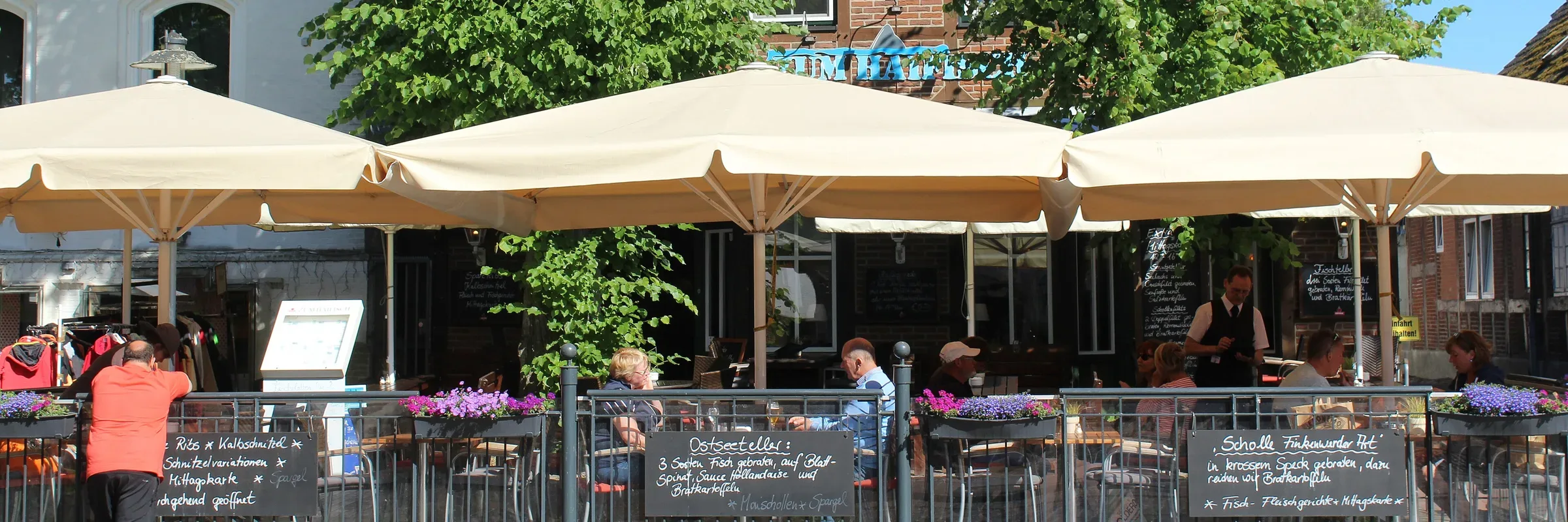 Restaurantterrasse mit Sonnenschirmen und Gästen in der Breiten Straße in Burg auf Fehmarn