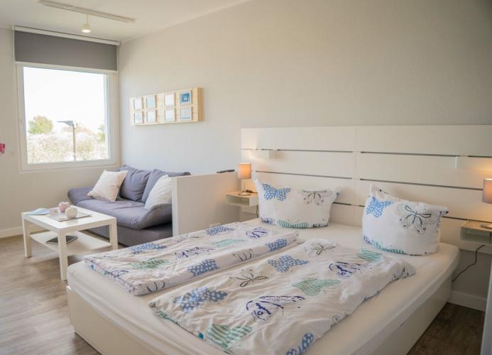 Doppelbett und gemütliche Couch in der Ferienwohnung mit Blick auf den Yachthafen auf Fehmarn